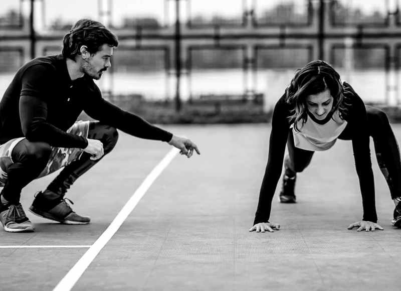 Young Female Athlete Exercising with Personal Fitness Trainer Young sporty woman exercising outdoors with personal fitness trainer